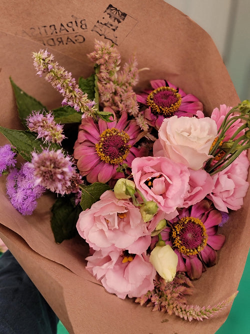 Bouquet of flowers wrapped in brown paper with a visible brand logo.