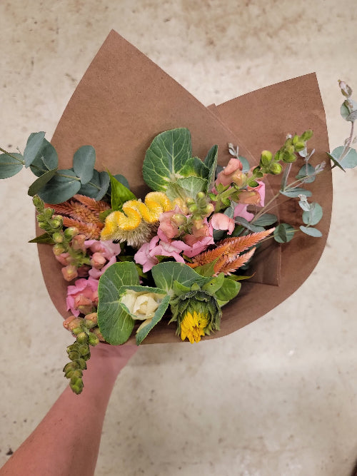 Bouquet of flowers wrapped in brown paper held by a hand on a light background
