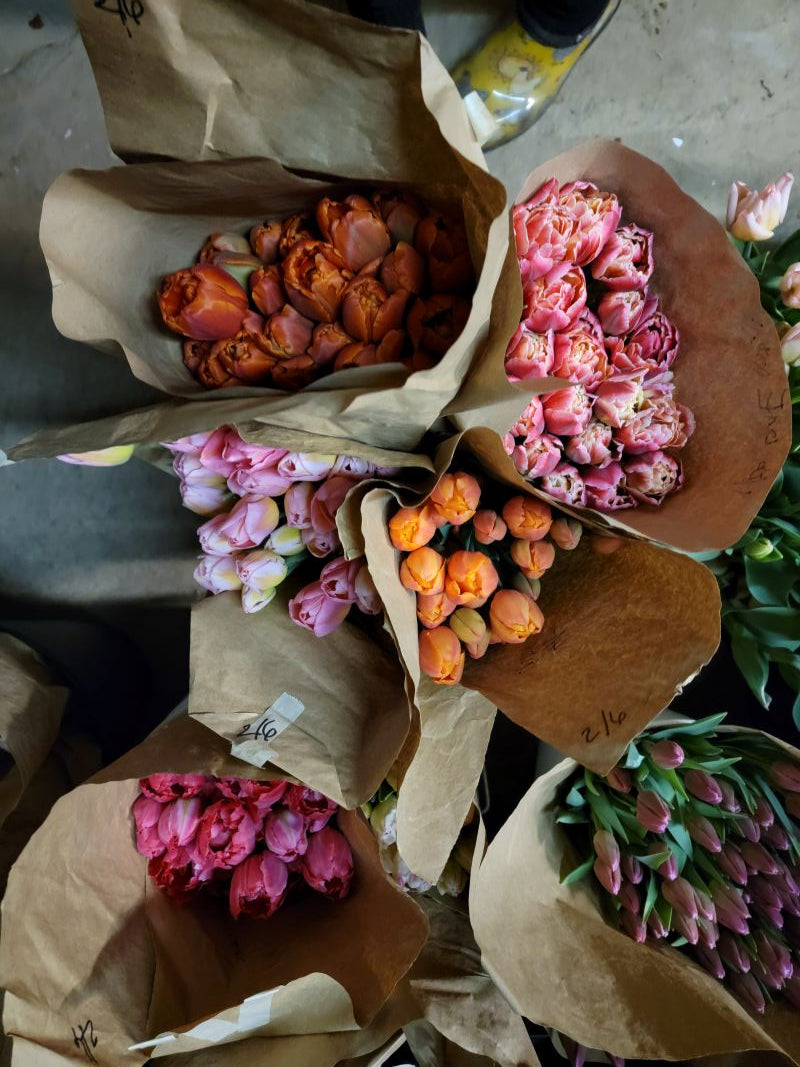 Bouquets of tulips in brown paper packaging on a concrete floor.