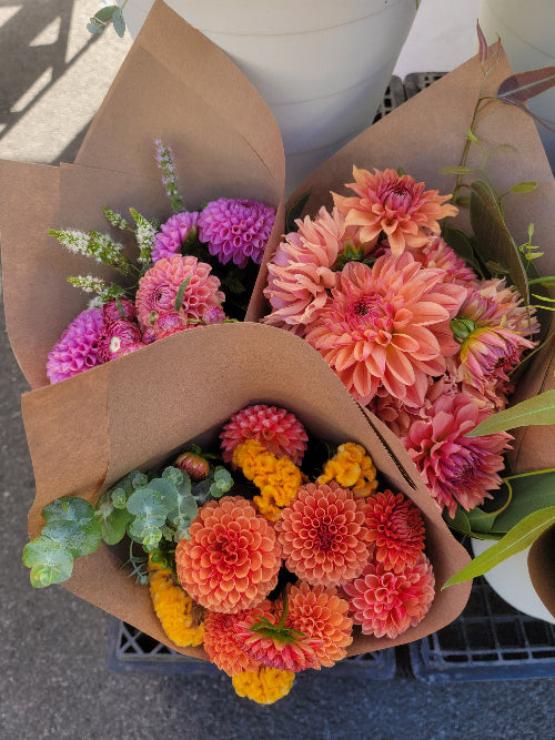 Bouquets of flowers wrapped in brown paper on a street.