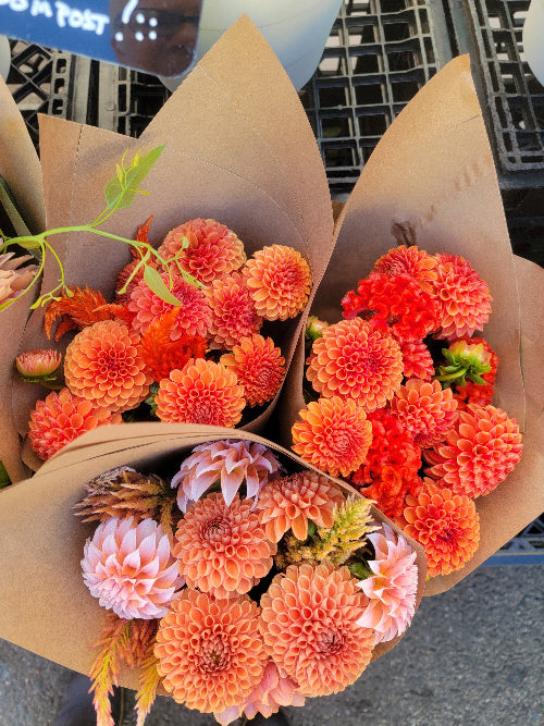 Bouquets of orange and pink flowers in brown paper packaging.