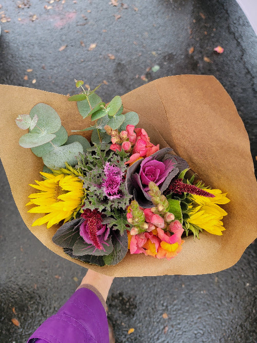 Bouquet of flowers wrapped in brown paper held by a person wearing purple pants.